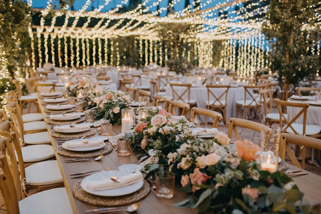 taula-llarga-decoracio-floral-cases-il·luminades Taula llarga amb decoració floral i il·luminació en un casament